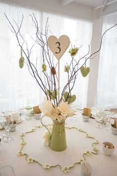 the table is set up for a wedding with white flowers and branches in a vase