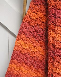 an orange and red crocheted scarf hanging from a hook on a white door