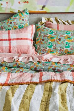 an unmade bed with colorful pillows and blankets on it's sides, in front of a painting