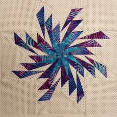 a quilted wall hanging with blue and purple strips on it's side, in the shape of a star