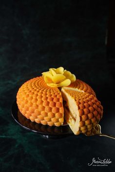 a cake on a black plate with a yellow flower on top and a fork in the foreground