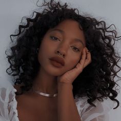 a woman with curly hair wearing a white shirt and posing for the camera while holding her hand to her face