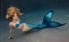 a woman in a blue and white mermaid costume is swimming under water with her hair blowing back