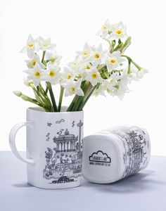 some white flowers are in a coffee cup and next to it is a canister