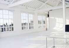 an empty white room with windows and a computer on a desk in front of it