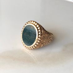 A vintage 9 carat gold bloodstone signet ring. The dark stone is held by a simple gold setting whilst the shoulders are decorating with a floral design. CONDITION: Good Condition, wear consistent with age and use. Please see photos for more detail. HALLMARKED, ASSAYED IN LONDON 1966  RING SIZE: UK: R 1/2 | US: 8 3/4 BAND WIDTH (NARROWEST POINT): 3mm FACE SIZE: 12mm x 15mm WEIGHT: 7.0 grams (VCZ) Antique Engraved Emerald Ring For Formal Occasions, Antique Gold Signet Ring With Gemstone, Victorian Gold Signet Ring With Gemstone, Gold Engraved Emerald Ring For Formal Occasions, Vintage Gold Ring For Memorial, Vintage Yellow Gold Oval Cabochon Signet Ring, Vintage Yellow Gold Signet Ring With Gemstone, Vintage Oval Cabochon Signet Ring For Formal Events, Vintage Oval Cabochon Signet Ring For Formal Occasions