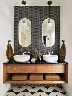 two sinks and mirrors in a bathroom with black and white tiles on the wall behind them