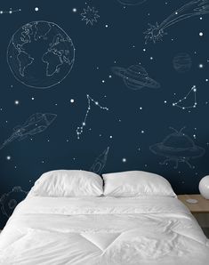 a bed with white sheets and pillows in front of a blue wall that has space drawings on it