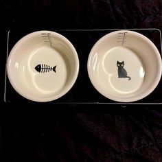 two white bowls with black cat and fish designs on the sides, one is empty