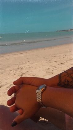 a person sitting on the beach with their arm wrapped around another person's wrist