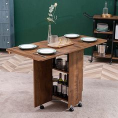 a table with plates and bottles on it in front of a green wall, next to a wine rack