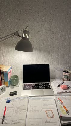 an open laptop computer sitting on top of a white desk next to books and papers