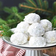 a white plate filled with snowball cookies on top of a table next to pine branches