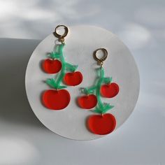 two red cherries hanging from green stems on a white plate with a gold hook