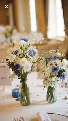 two vases filled with white and blue flowers sitting on top of a dining table