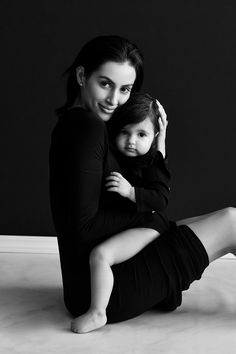 a woman sitting on the floor holding a small child in her lap and posing for a black and white photo