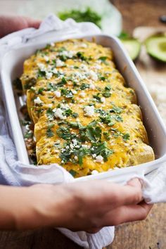 someone is holding a casserole dish with cheese and cilantro on it