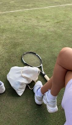 a woman sitting on top of a tennis court holding a racquet next to a bag