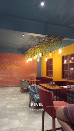 the interior of a restaurant with yellow walls and wooden tables, red chairs, and hanging plants