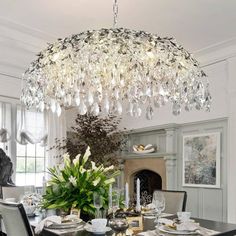 a chandelier hanging over a dining room table with place settings on the side