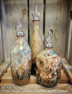 three brown and blue vases sitting on top of a wooden shelf next to each other