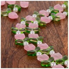 some green and pink glass beads on a wooden table with pearls in the middle of them