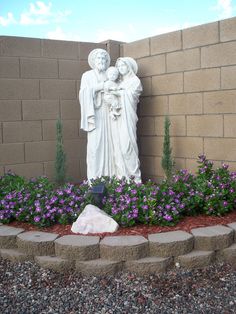 a garden with flowers and a statue in the middle, along side a brick wall