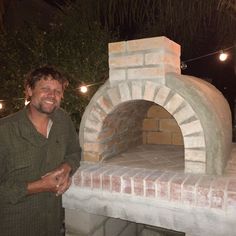 a man standing in front of an outdoor brick oven with lights on the outside wall