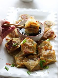 a person holding chopsticks over some food on a white plate with sauce in it