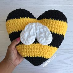 a hand holding up a crocheted heart with two white circles on it and a black and yellow stripe