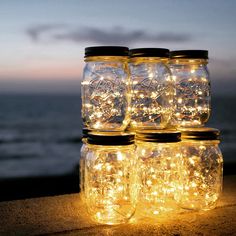 mason jars filled with fairy lights sitting on top of a wooden table next to the ocean