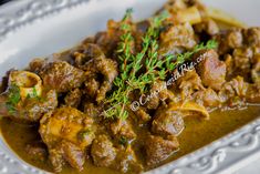 a white plate topped with meat covered in gravy and garnished with parsley