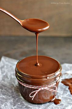 a spoon full of chocolate spread on top of a jar filled with caramel sauce