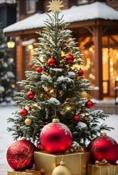 a small christmas tree with red and gold ornaments in front of a building on a snowy day