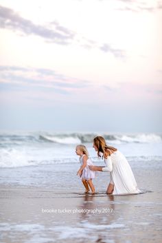 a mother and her daughter playing on the beach at sunset with waves in the background