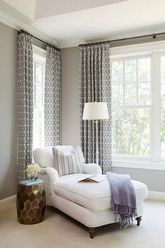 a white couch sitting in front of a window next to a table with a lamp on it