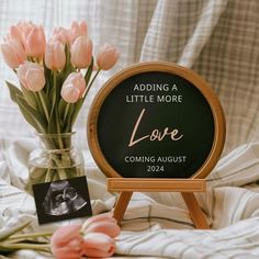 a vase filled with pink flowers next to a sign that says, adding a little more love coming august