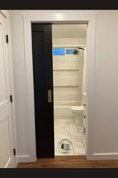 an open door leading to a bathroom with white walls and tile flooring in it