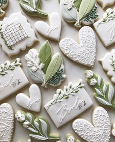 many decorated cookies are arranged on a white tablecloth with green leaves and flowers in the shape of hearts