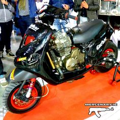 a black motorcycle parked on top of a red carpet next to people standing around it