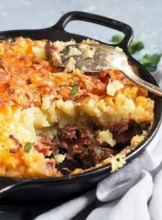 a casserole dish with meat and vegetables in it on a white cloth next to a spoon