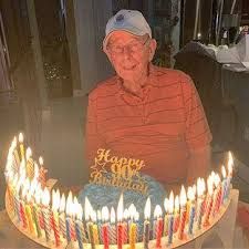 an old man sitting in front of a birthday cake with lit candles on it,