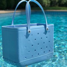 a blue tote bag sitting on top of a swimming pool next to a green tree