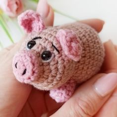 a small crocheted pig is held in someone's hand next to flowers