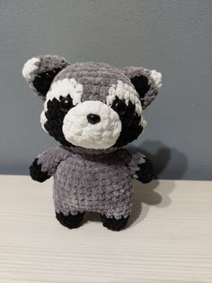 a crocheted raccoon stuffed animal sitting on top of a wooden table