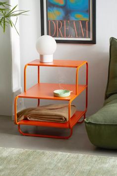 an orange shelf sitting on top of a green couch next to a white vase and potted plant