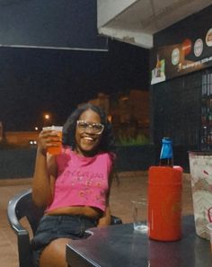 a woman sitting at a table with a drink in her hand and a soda bottle next to her