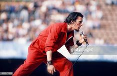 a man in red jumpsuits holding a microphone and singing into a mic on stage