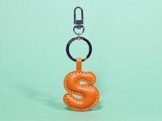 an orange leather keychain with the letter s on it, hanging from a metal hook