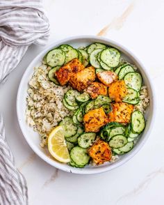 a white bowl filled with rice, cucumbers and chicken on top of it